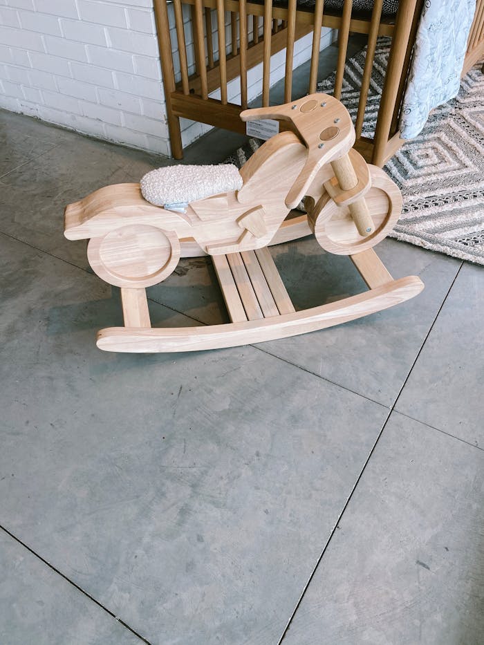 Wooden rocking motorcycle toy in a cozy nursery setting on a tiled floor.